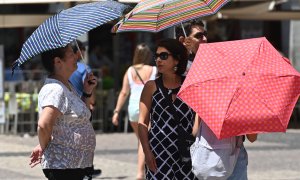 Varias personas caminan con sombrilla por el centro de Madrid.