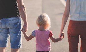 Imagen de una madre y un padre cogiendo de la mano a su hija.