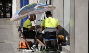 Dos operarios de telefonía se protegen con una sombrilla del intenso sol y calor en Valencia.