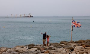 Un hombre y una niña observan desde la orilla, junto a una bandera británica, al granelero OS35, medio hundido frente a Gibraltar. REUTERS/Jon Nazca