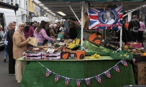 Día de mercado, una mujer mira a la cámara desde un puesto de frutas en la periferia londinense.