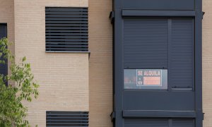 En la fachada de un edificio se ve un cartel de 'Se Alquila' bajo la persiana de uno de los pisos.