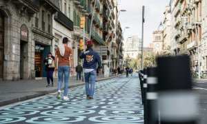 Pla general de dos homes caminant pel carrer Pelai, amb l'espai per a vianants pintat amb panots blaus, en una imatge d'arxiu