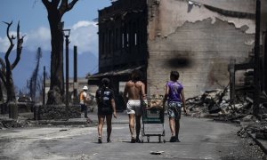 11/08/2023 - Tres residentes empujan un carrito en medio de las ruinas provocadas por el incendio forestal que arrasó la ciudad hasta la costa y el puerto en Hawái, a 11 de agosto de 2023.