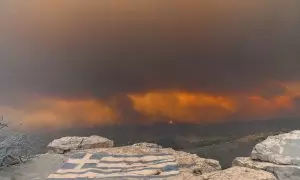 Una bandera griega pintada en la zona de Makri con un fondo de los incendios forestales alrededor de Alexandroupolis, Tracia, en el norte de Grecia, el 22 de agosto de 2023.