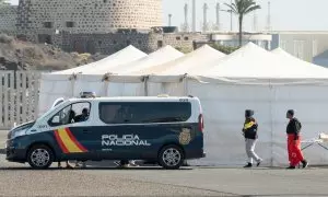 Tres mujeres pasan ante un coche de policía y las carpas del campamento provisional en Arrecife.