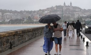 Dos personas se protegen de la lluvia con un paraguas en la playa de Ondarreta, a 14 de octubre de 2023, en San Sebastián