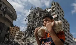 16/10/23 Un joven palestino porta dos bolsas de pan este lunes 16 de octubre frente a un edificio bombardeado en el barrio de Al Remal, en la ciudad de Gaza.