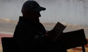 Un anciano lee un libro en un banco de un parque en Madrid.