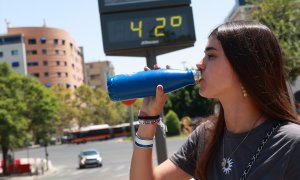 14/08/2024 Una joven bebe agua en la calle en Sevilla este agosto. Al fondo, un termómetro.