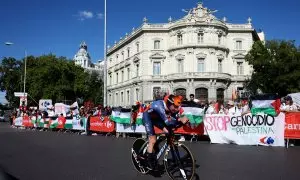 Un ciclista del equipo Jayco AlUla pasa junto a personas con banderas y pancartas en apoyo a los palestinos en Gaza, en la última etapa de la Vuelta a España, en la madrileña Plaza de Cibeles