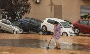 Una mujer realiza labores de limpieza junto a vehículos destrozados tras el paso de la DANA por el barrio de La Torre de València, a 30 de octubre de 2024.